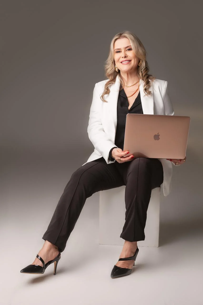 Dra. Gláucia Messa de blazer branco, sentada com um notebook